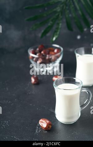 Ramadan Kareem Essen und Getränke. Teller mit Datteln, Glas Milch und Dattelpalmzweig auf schwarzem Hintergrund. Gerechter Muslimischer Lebensstil. Vegetarische Gerichte. S Stockfoto