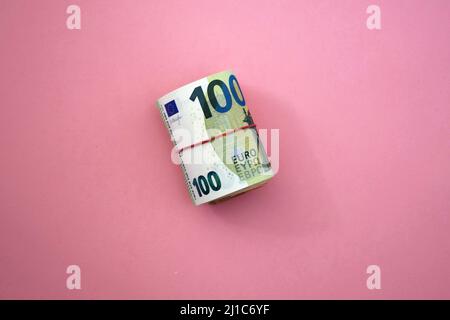 Rolle der Euro-Banknoten. 100 Euro mit rotem Gummiband auf rosa Hintergrund. Unternehmen, Finanzen, Währung Stockfoto