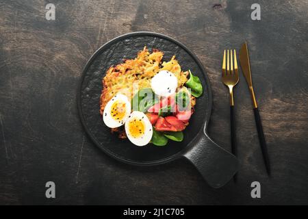 Kartoffeln latkes mit Sauerrahm, Spinatsalat, Tomaten und gekochten Eiern auf dunklem Holz alten Tischhintergrund. Hausgemachte leckere Kartoffelpfannkuchen. Deliciou Stockfoto