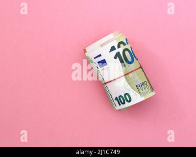 Rolle der Euro-Banknoten. 100 Euro mit rotem Gummiband auf rosa Hintergrund. Unternehmen, Finanzen, Währung Stockfoto