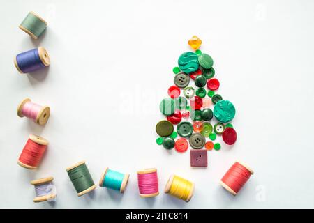 Baum aus Knöpfen grün, rote Farbe. Mehrfarbige Fäden mit Holzspulen. Weißer Hintergrund, Kopierbereich. Kreatives Weihnachtskonzept oder Gartenarbeit Stockfoto