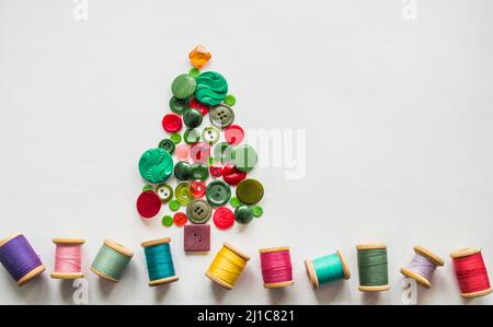 Baum aus Knöpfen grün, rote Farbe. Mehrfarbige Fäden mit Holzspulen. Weißer Hintergrund, Kopierbereich. Kreatives Weihnachtskonzept oder Gartenarbeit Stockfoto