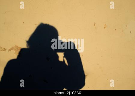 Selfie einer Fotografin in Form eines menschlichen Schattens mit einer Kamera auf einem gelben alten schäbigen Wandhintergrund. Speicherplatz kopieren. Stockfoto