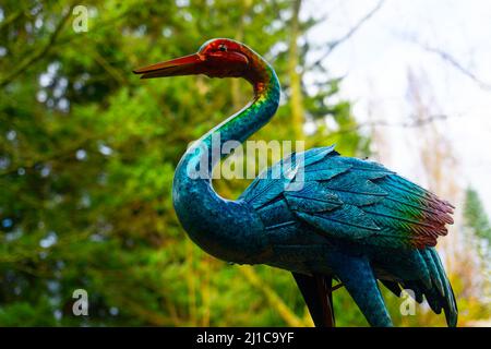 Ein Vogel, der eine klare Mischung aus einem Falmingo und einem Kranich hat, sitzt in einem Hof als Dekoration vor einer baumgefüllten Kulisse. Stockfoto