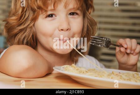 Kaukasisch lächelndes Kind, das Pasta, Spaghetti isst, Nahaufnahme eines Porträts. Kindergesicht. Stockfoto