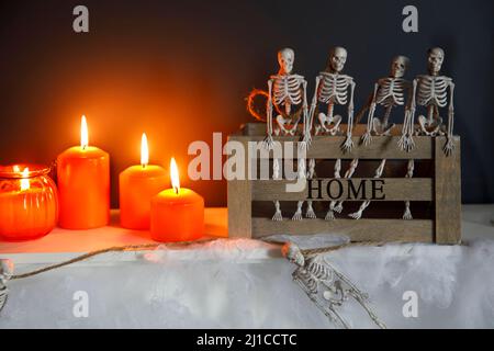 Halloween-Heimtextilien. Plastikspielzeug-Skelette in Holzkiste am Kamin vor einer dunkelblauen Wand. Eine Girlande aus Skeletten. Spinnennetz auf der Kommode. O Stockfoto