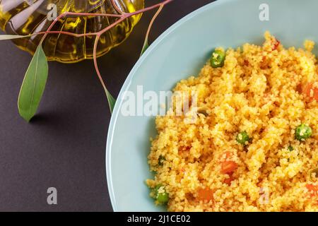 Couscous ist ein nationales nordafrikanisches Gericht aus Weizengroats. Couscous mit Gemüse in einer Schüssel mit Olivenöl und einem Zweig mit Blättern auf einem schwarzen Stockfoto