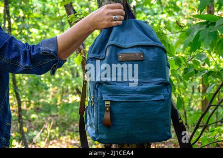 Touristenwanderung durch den Sommerwald. Weibliche Hand hält einen blauen Rucksack. Ein schöner silberner Ring mit einem blauen Stein an einem Finger. Nahaufnahme. Selektiv Stockfoto