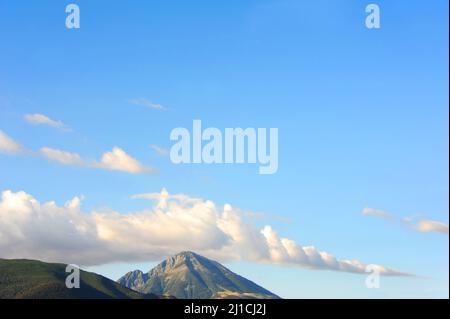 Der wunderschöne Gipfel erhebt sich über dem Absaroka Mountain Range in Montana. Dieser Hintergrund wird von einem leuchtend blauen Himmel und Wolken ausgefüllt. Stockfoto