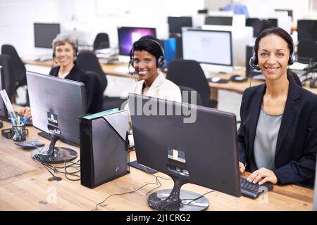 Sie sind das beste Team im Call Center. Eine kurze Aufnahme von drei Callcenter-Sprecherinnen, die Headsets tragen. Stockfoto