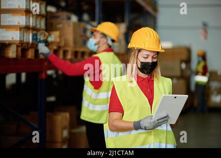 Kaukasische Arbeiterin prüft die Bestellung in einem Lager während Tragen einer Gesichtsmaske - Gesichtsfokus Stockfoto