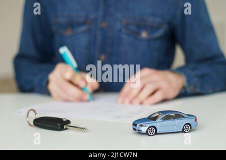 Junger Mann, der auf dem Hintergrund Kfz-Versicherungsdokumente unterschreibt. Stockfoto