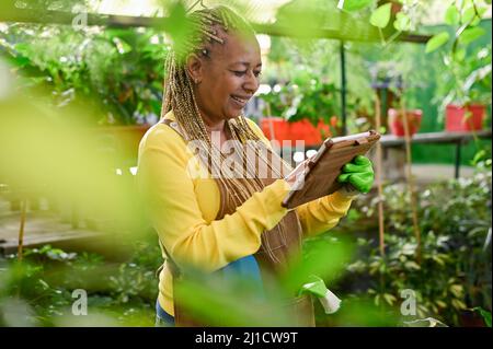 Glänzende schwarze Frau mit Tablette im Gewächshaus Stockfoto