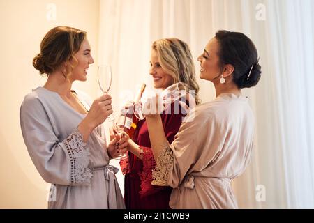 Ein wenig Champagner macht das. Eine kurze Aufnahme einer schönen jungen Braut und ihrer Brautjungfern, die vor der Hochzeit Champagner in ihrem Ankleidezimmer hatten. Stockfoto