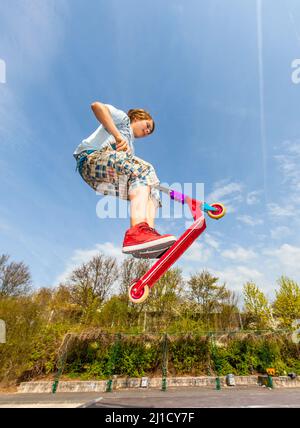 Junge springt mit einem Motorroller über einen Dorn in den Skate Park und genießen es Stockfoto