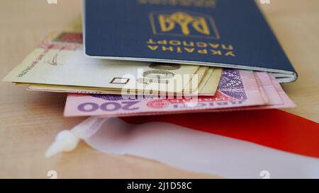 Nahaufnahme eines biometrischen ukrainischen Reisepasses mit Griwna-Banknoten auf dem Hintergrund der polnischen Flagge.das Konzept des Wechsels in einem anderen Land Stockfoto