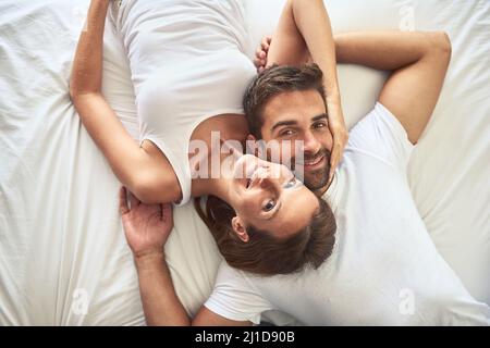 Unser Aufenthalt im Bett war den ganzen Tag über ein Gesicht. High-Angle-Aufnahme eines glücklichen jungen Paares, das sich zu Hause im Bett entspannt. Stockfoto