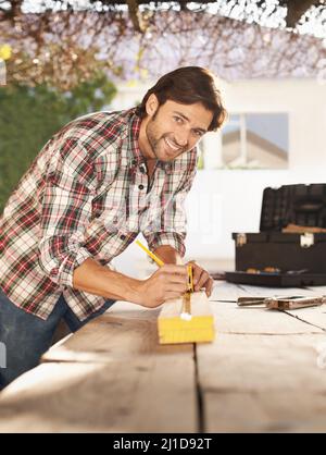 Ich liebe DIY. Ein hübscher junger Zimmermann, der etwas Holz misst. Stockfoto