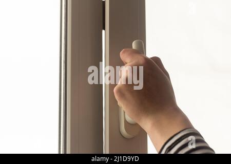 Eine Hand öffnet ein Fenster in einer Wohnung oder einem Haus zur Belüftung Stockfoto