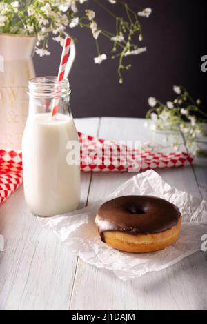 Hausgemachter Donut mit Schokoladenglasur und Glas Milch auf weißer rustikaler Holzoberfläche bedeckt Stockfoto