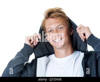 In der Haube. Ein junger rotköpfiger Mann hebt seinen Hoodie über seinen Kopf, während er die Kamera anlächelt. Stockfoto