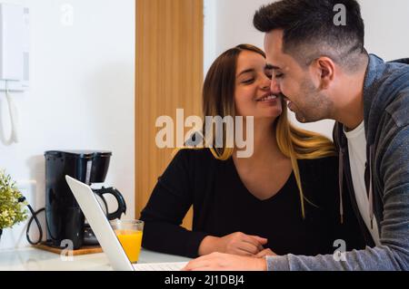 Heterosexuelles junges kaukasisches Paar, das sich über ihre Einnahmen aus Online-Investitionen freut, bärtige Männer und Frauen, die zusammen lächeln und sich auf das Coun stützen Stockfoto
