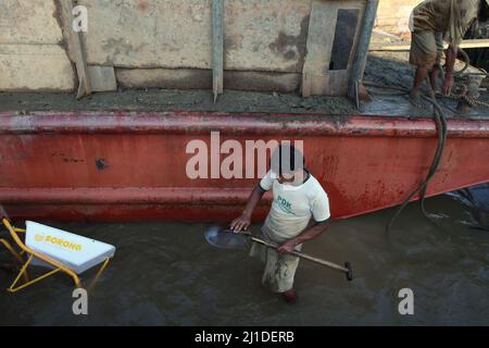 Ein Arbeiter reinigt seine Schaufel, nachdem er Sand von einem Lastkahn entladen hat, während er auf flachem Wasser am Ufer des Musi-Flusses in Süd-Sumatra, Indonesien, steht. © Reynold Sumayku Stockfoto