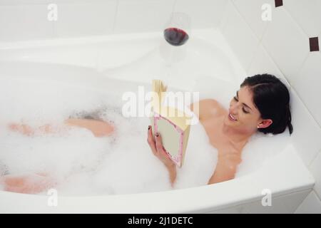 Entspannen in der Badewanne. Eine kleine Aufnahme einer jungen Frau, die sich mit einem Buch und einem Glas Wein in der Badewanne entspannt. Stockfoto