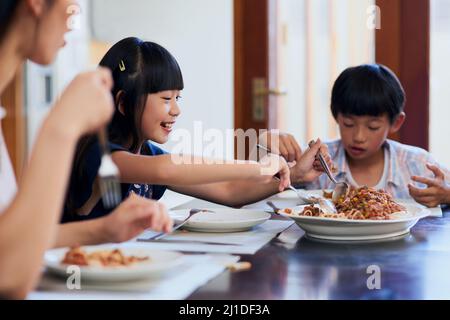 Ich bin Sekunden lang da. Aufnahme von zwei kleinen Kindern, die mit ihrer Mutter zu Hause essen. Stockfoto