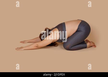 Übergewichtige fette Frau mit massiven Schultern in grauer Sportuniform bereit für Gymnastik, Pilates, Yoga. Fetalposition Stockfoto