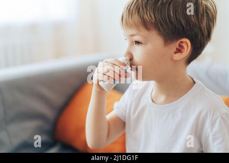 Der kleine Junge verwendet hormonelles Nasenspray, während er auf der Couch sitzt Stockfoto