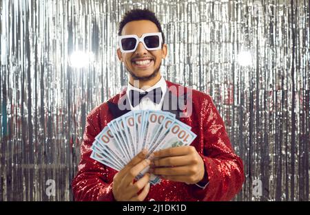 Glücklicher schwarzer Kerl, der viel Geld gewonnen hat, indem er einen Haufen Banknoten hält und lächelt Stockfoto