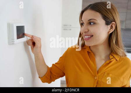 Porträt einer lächelnden Frau senkt die Temperatur auf dem digitalen Thermostat zu Hause. Energiesparende, effiziente und intelligente Technologie. Stockfoto