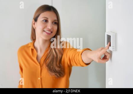 Senken der Temperatur zur Energieeinsparung. Junge Frau, die zu Hause den digitalen Thermostat für die Zentralheizung justiert. Konzentrieren Sie sich auf die Hand. Stockfoto