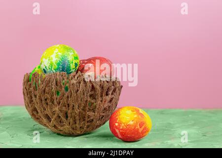 Bunte Eier im Nest auf grünem und rosa Hintergrund. Ostern. Speicherplatz kopieren Stockfoto
