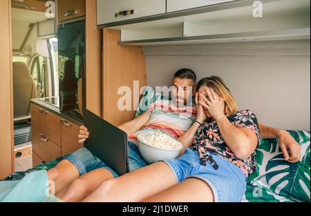 Junges Paar, das sich einen unheimlichen Film auf dem Tablet ansieht, das auf dem Bett ihres Wohnwagens liegt. Stockfoto