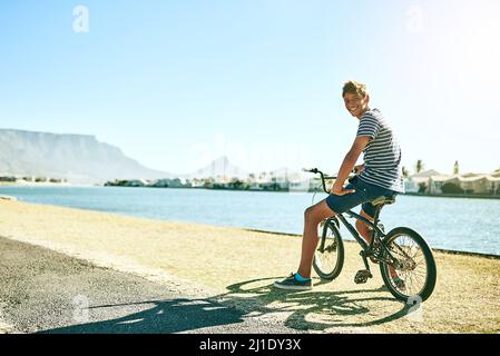 Du willst für eine Fahrt kommen. Porträt eines jungen Jungen, der mit dem Fahrrad an einer Lagune entlang fährt. Stockfoto