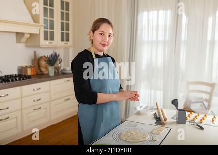 Die junge zentralasiatische Frau backt im Inneren einer modernen Küche. Stockfoto