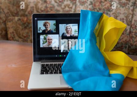 Flagge der Ukraine auf dem Hintergrund und breiten digitalen Bildschirm des Laptops mit Videokonferenz. Krieg mit Russland. Cyberangriff, Sanktionen, wirtschaftlicher Zusammenbruch Stockfoto