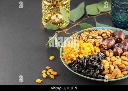 Ramadan-Konzept. Nüsse, getrocknete Früchte und Datteln in der blauen Schale, Glas Wasser und ramadan-Laterne auf schwarzem Hintergrund mit Kopierraum. Arabisches Gericht, s Stockfoto