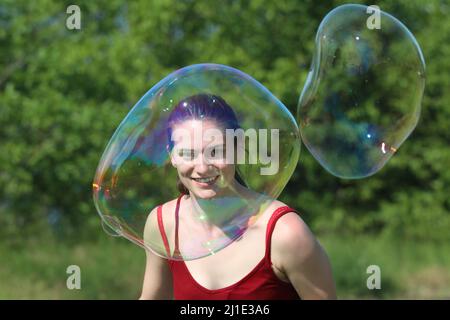 04.06.2021, Deutschland, , Berlin - Teenager, die glücklich durch eine große Seifenblase zum Betrachter schauen. 00S210604D232CAROEX.JPG [MODELLVERSION: NEIN, EIGENTUM Stockfoto