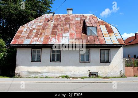 Vorderansicht eines verlassenen kleinen städtischen Familienhauses auf einem rissigen Stein- und Betonfundament mit beschädigter Fassade um alte Fenster mit verfallener Holzkonstruktion Stockfoto