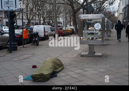 05.02.2022, Deutschland, , Berlin - Ein Obdachloser schläft in seinem Schlafsack auf dem Bürgersteig vor einem Modehaus am Kurfürstendamm. 0SL220205D00 Stockfoto