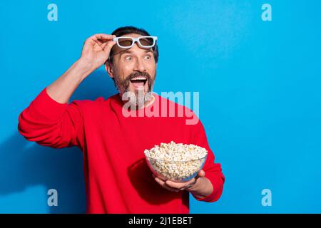 Portrait von attraktiven fröhlichen Mann essen Mais beobachten Video Spaß isoliert über hellen blauen Hintergrund Stockfoto