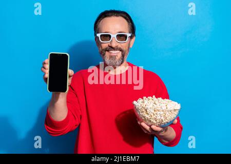 Foto von lachenden guten Laune Mann Werbung Telefon Film Film isoliert auf blauem Hintergrund zu sehen Stockfoto