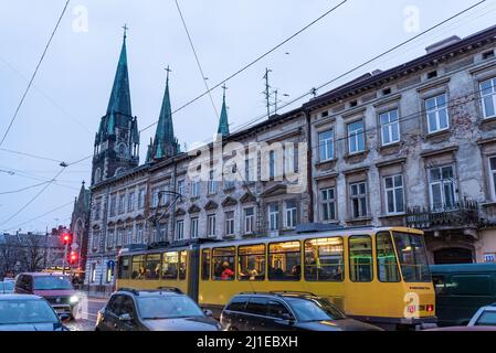 11. März 2022, Lemberg, Ukraine. Straßenbahn von Lemberg öffentlichen Verkehrsmitteln ist im Verkehr in der Innenstadt mit Denkmal und Kirche im Hintergrund gesehen Stockfoto