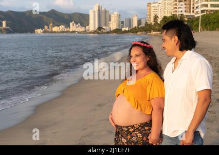 Junge schwanger Paar zu Fuß am Strand Stockfoto
