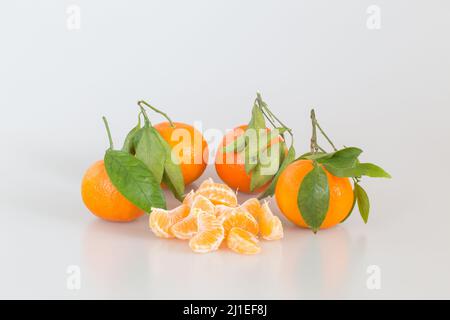 Reife Mandarinen mit grünen Blättern und Scheiben. Orange Zitrusfrüchte isoliert auf weißem Hintergrund. Stockfoto