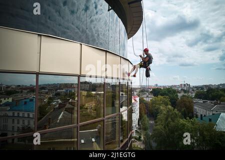 Industrieller Bergsteiger, der Glasfenster des Hochhauses reinigt. Männlicher Reiniger, der beim Waschen der Fenster des Wolkenkratzers Sicherheitsausrüstung verwendet. Stockfoto