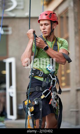 Industriebergsteiger Arbeiter in Schutzhelm hält Kletterseil und steht vor dem Gebäude auf verschwommenem Hintergrund. Mann, der Sicherheitshebevorrichtung verwendet. Stockfoto